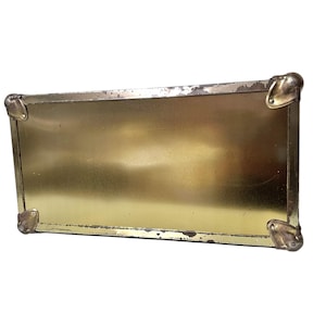 Op de afbeelding: Een rechthoekig, goudkleurig metalen bord met afgeronde hoekbeschermers. Het bord heeft een licht verweerde uitstraling, met wat slijtage zichtbaar rond de randen. De hoekbeschermers zijn van een donkerdere goudkleur.