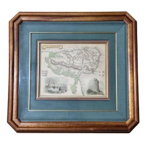 May include: Framed antique map print of a city, featuring a detailed cartographic illustration with green and gray tones. The map is set within a teal mat and a gold inner frame, encased in a dark wood frame.