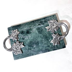 May include: A rectangular serving tray with a green marble surface and silver-colored handles. The handles are designed with a leaf motif. The tray is ideal for serving appetizers or displaying decorative items.