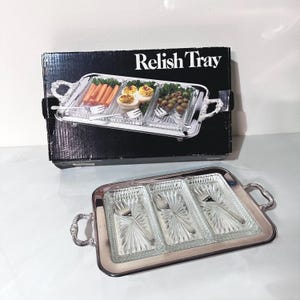 May include: A silver-toned relish tray with three glass compartments and ornate handles. The box behind it reads "Relish Tray". The tray is designed to hold appetizers, with a fork in each compartment.