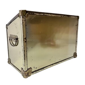 Op de afbeelding: Een vintage metalen koffer met een rechthoekige vorm, cr&egrave;me geschilderd met messing hoekbeschermers en een handvat. Het metaal vertoont tekenen van slijtage, wat het een rustieke uitstraling geeft. Afmetingen: ongeveer 40 cm x 25 cm x 20 cm.
