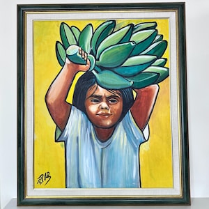 May include: A framed painting depicts a young person carrying a large bunch of green bananas on their head. The person is wearing a light blue shirt against a yellow background. The artwork is signed in the lower left corner and framed in a dark green frame.