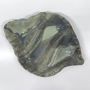 May include: A handmade ceramic leaf-shaped dish with a glossy finish. The dish features a blend of muted colors, including shades of gray, blue, and green. The edges have a slightly irregular shape, adding to its unique, organic aesthetic.