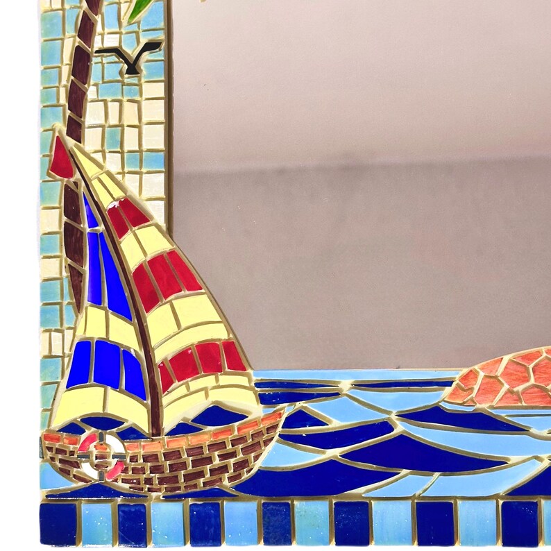 May include: A mosaic mirror with a nautical theme. The frame features a sailboat with red, yellow, and blue sails, set against a blue ocean. A palm tree and a bird are also depicted in the mosaic design.
