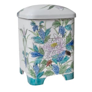 May include: A white, tiered ceramic box with a lid, featuring hand-painted floral designs. The box has a square shape with rounded edges and is decorated with pink, blue, and green flowers and leaves. The base has a turquoise geometric pattern.