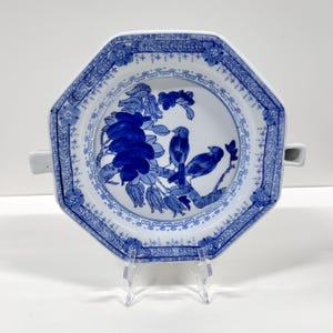 May include: An octagonal, white porcelain plate with a blue floral and bird design. The plate features a detailed border and two small handles. The central design depicts blue birds perched on a flowering branch. A decorative piece for serving or display.