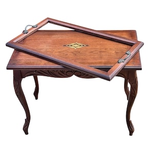 May include: A rectangular wooden side table with curved legs and carved detailing, featuring a matching wooden serving tray with metal handles and a central geometric inlay resting diagonally across the tabletop surface.