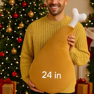 Könnte beinhalten: Ein großes, senffarbenes Truthahnbein-Kissen, etwa 61 cm lang, wird von einer Person gehalten. Das Kissen hat ein weißes Knochen-Detail. Im Hintergrund ein geschmückter Weihnachtsbaum und verpackte Geschenke.