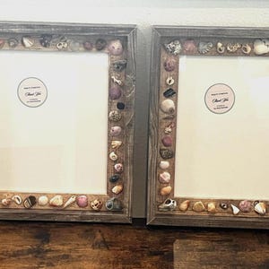 May include: Two rectangular picture frames with dark brown weathered wood borders decorated with an assortment of natural seashells in various shapes, sizes, and colors. Each frame contains a white mat with a circular Thank You sticker.