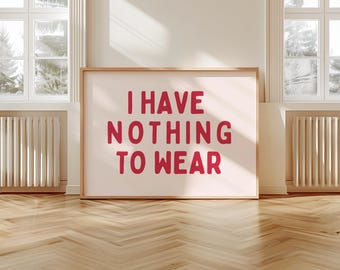 May include: A framed print with the text "I HAVE NOTHING TO WEAR" in bold, red letters. The artwork is displayed on a light-colored wall, with a wooden frame. The room has hardwood floors and large windows.