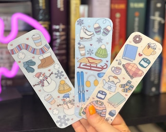 May include: Three colorful bookmarks with winter-themed illustrations. The bookmarks feature a snowman, a winter scene with skis, and a cozy scene with a teapot and a book.