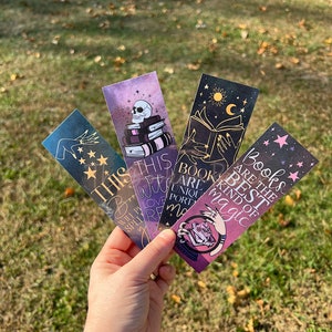 May include: Four colorful bookmarks with a magical theme. The bookmarks feature illustrations of a skull, a hand holding a book, a crystal ball, and a book with stars. The text on the bookmarks reads "This Witch Will Put A Spell On You", "Books Are Unique Portals To Magic", and "Books Are The Best Kind Of Magic".