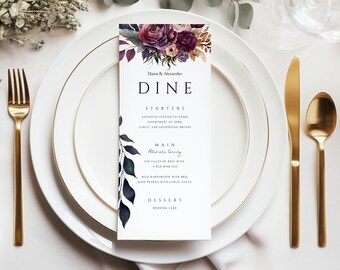 Op de afbeelding: Een huwelijksmenukaart met een bloemmotief in tinten paars, roze en blauw. De tekst op de kaart luidt "Diana & Alexander Dine" en vermeldt de voorgerechten, het hoofdgerecht en het dessert.