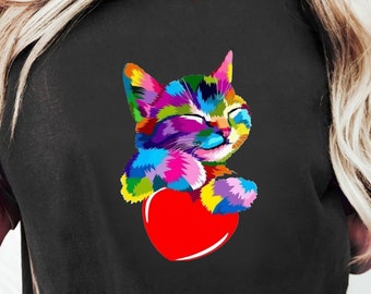 Puede incluir: Una camiseta negra con una ilustración colorida de un gato sosteniendo un corazón rojo. El gato está hecho de varios colores, incluyendo rosa, azul, verde y amarillo.