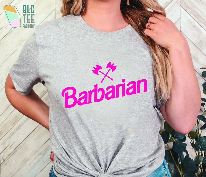 May include: A gray t-shirt with a pink graphic of crossed axes and the word "Barbarian" in a bold, pink font.