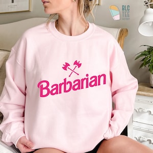 May include: Pink sweatshirt with a pink graphic of crossed axes and the word "Barbarian" in a bold, stylized font.