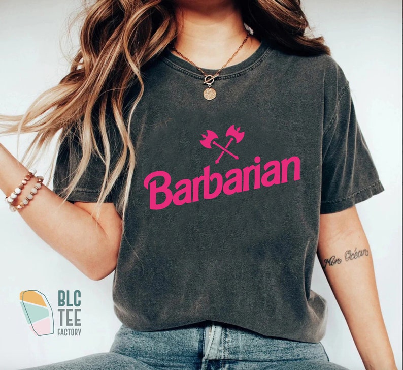 May include: A dark gray t-shirt with a pink graphic of crossed axes and the word "Barbarian".