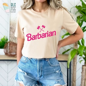 May include: A beige t-shirt with a pink graphic of crossed axes and the word "Barbarian".