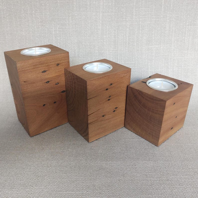 May include: Three rectangular wooden candle holders of varying heights, each featuring a natural brown wood grain with visible knots and a circular silver metal insert at the top designed to hold a standard tea light candle securely in place.
