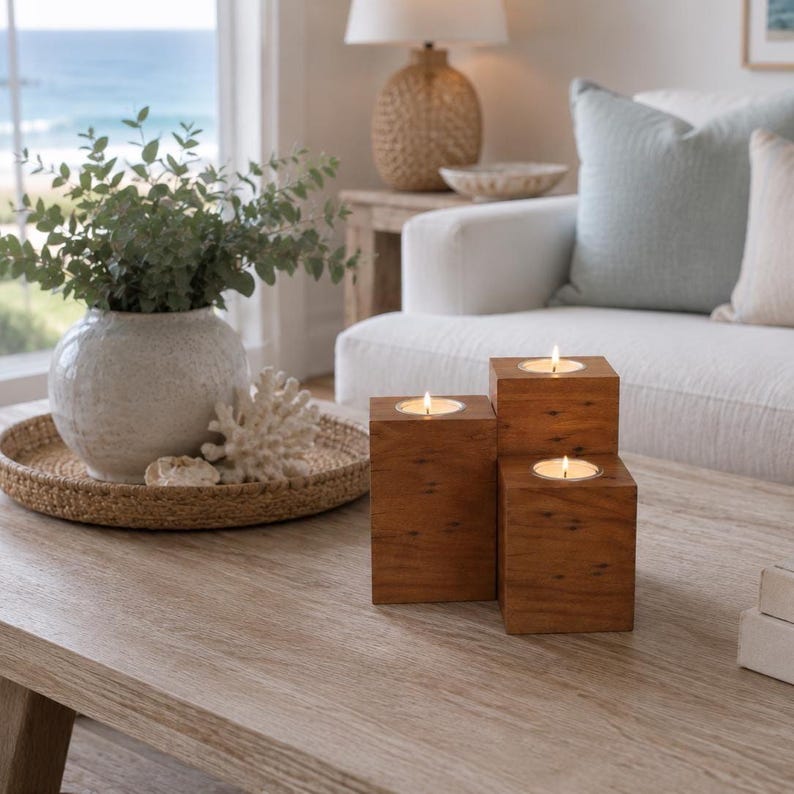 May include: A set of three square wooden candle holders of varying heights, each featuring a single lit tea light candle. The natural brown wood grain is visible on the surfaces of the blocks, which are arranged in a cluster on a light wood table.