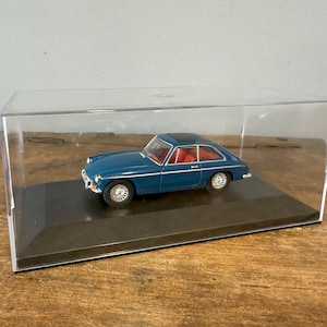 Puede incluir: Un coche modelo azul en una vitrina de plástico transparente. El coche tiene un interior negro y un interior rojo. El coche está sentado sobre una base negra.