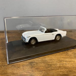 Puede incluir: Modelo de coche blanco convertible en una vitrina transparente con una base negra.