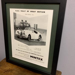 Peut inclure: Une photo en noir et blanc d'une Jaguar XK 120 blanche de course participant au rallye R.A.C. de Grande-Bretagne en mars 1953. La voiture est conduite sur une route de terre avec une voiture plus petite en arrière-plan. Le texte "All these cars were fitted with MINTEX brake liners" est imprimé en bas de la photo.