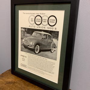 May include: A black and white vintage advertisement for the Auto Union 1000 S car. The ad features a photo of the car and text that highlights its safety, sports car performance, spacious comfort, and outstanding appearance. The ad also includes the text "Stand 125 at the Motor Show".