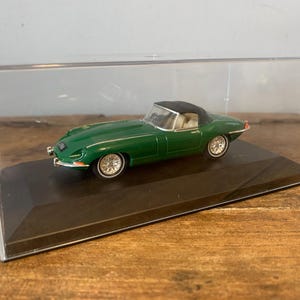 Puede incluir: Un coche modelo verde de fundición a presión en una vitrina transparente. El coche es un descapotable con capo negro y ruedas cromadas.