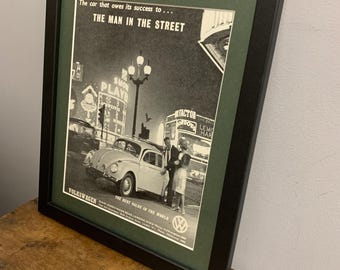 Peut inclure: Une publicité vintage en noir et blanc pour la Volkswagen Beetle. La publicité présente une photo d'une Volkswagen Beetle roulant dans une rue de la ville la nuit. Le texte de la publicité dit "La voiture qui doit son succès à... L'HOMME DE LA RUE" et "VOLKSWAGEN LA MEILLEURE VALEUR AU MONDE".