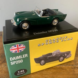 Puede incluir: Un coche modelo verde Daimler SP250, escala 1:43, sobre un soporte negro. La caja muestra la bandera británica, las palabras "Daimler SP250" y "Classic Sports Cars". El modelo es un descapotable clásico.
