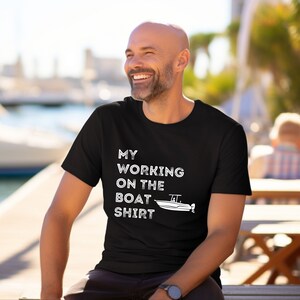 May include: A black t-shirt with the text 'My Working On The Boat Shirt' in white text. A small white boat graphic is next to the text.