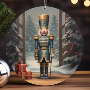 May include: A round Christmas ornament featuring a blue and gold toy soldier standing in front of a snowy winter scene. The soldier is holding a staff and has a red and white hat.