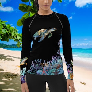 Op de afbeelding: Een witte keramische mok met een zwarte handgreep en de tekst "But First, Coffee" in een vetgedrukte, zwarte letter. De mok staat tegen een vage achtergrond. De mok is ongeveer 10 cm hoog.