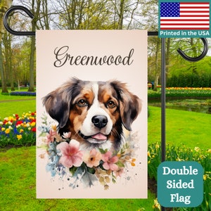 May include: A double-sided garden flag featuring a watercolour painting of a brown and white dog with pink flowers. The flag has the text "Greenwood" at the top.