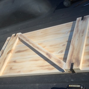 May include: A wooden door with a diagonal brace and black metal hinges. The door is made of light wood with a natural finish.