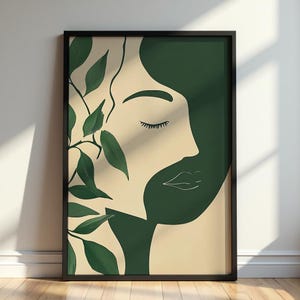 Peut inclure: Une affiche encadrée présentant une illustration minimaliste d'un profil de femme. L'œuvre utilise une palette de crème, de vert foncé et de noir. Une branche feuillue est sur le côté gauche du visage. Le visage de la femme est de profil, les yeux fermés et une expression douce.