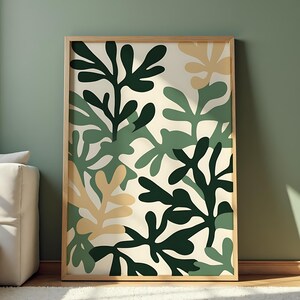 Könnte beinhalten: Ein gerahmter Kunstdruck mit einem botanischen Design. Das Kunstwerk zeigt stilisierte Blattformen in Grün- und Beigetönen vor einem cremefarbenen Hintergrund. Der Holzrahmen verleiht der modernen Wanddekoration eine natürliche Note.