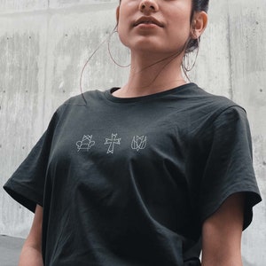 Könnte beinhalten: Ein schwarzes T-Shirt mit einem weißen grafischen Design aus einem Stuhl, einem Kreuz und einer Blume. Das Design ist schlicht und minimalistisch.