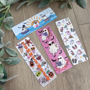 May include: Four rectangular bookmarks featuring cartoon ghosts in summer settings. One shows ghosts at the beach, another has a pink background with ghosts reading, one features a pattern of summer icons, and one displays the word SUMMERWEEN.