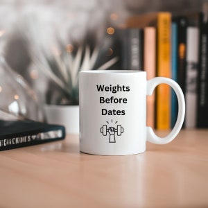 May include: White ceramic mug with a black graphic of a hand lifting a dumbbell. The text on the mug reads "Weights Before Dates."
