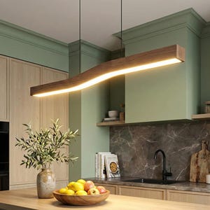May include: A modern kitchen with a wooden light fixture. The light fixture is a long, wavy shape with a bright, warm light. The kitchen has light-colored wooden cabinets and a green wall. A wooden bowl of fruit sits on the countertop.