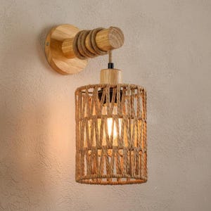 Könnte beinhalten: Eine Wandleuchte mit einem natürlichen, rustikalen Design. Sie verfügt über einen Holzsockel und -arm mit einem zylindrischen Lampenschirm aus Seil. Das Licht ist warm und einladend, perfekt, um einen Hauch von naturnaher Dekoration zu verleihen.