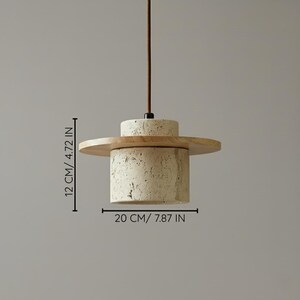 Puede incluir: L&aacute;mpara colgante moderna con base cil&iacute;ndrica de piedra beige texturizada, pantalla circular de madera y parte superior de piedra m&aacute;s peque&ntilde;a. La base mide 20 cm de ancho y 12 cm de alto.