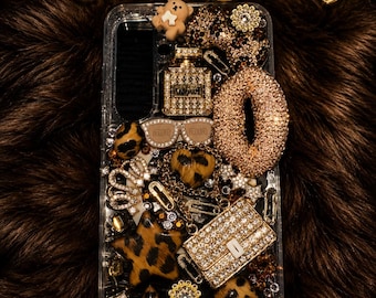 May include: A clear phone case decorated with gold-toned charms, leopard print accents, a rhinestone-encrusted handbag, a perfume bottle, sunglasses, a teddy bear, and the word Love in script. The text Kreative Juicez appears above.