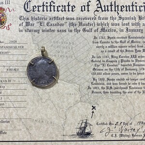 May include: A certificate of authenticity for an 8 Reale Spanish silver coin from 1773. The coin features the image of King Carolus III and is described as a "Piece of Eight". The certificate includes a map of the Gulf of Mexico and a small illustration of a ship.