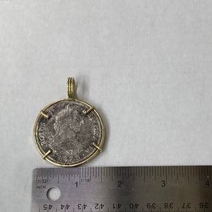 May include: A silver coin with a gold rim and a gold bail. The coin features a portrait of a man with a crown and the text "ROLUS GR" on the edge. The coin is about 1 inch in diameter.