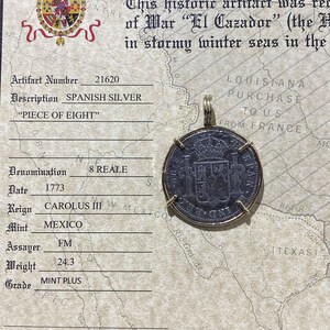 May include: A certificate of authenticity for a Spanish silver "Piece of Eight" coin, dated 1773. The coin is 8 reales and was minted in Mexico during the reign of Carolus III. The certificate includes the coin's artifact number, denomination, date, reign, mint, assayer, weight, and grade. The coin is pictured on the certificate.