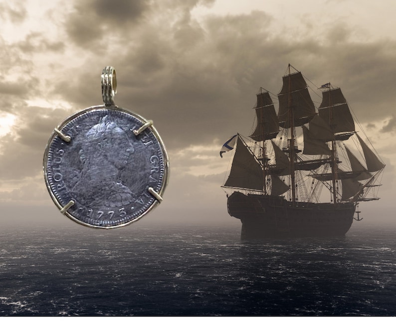 May include: A silver coin pendant with a portrait of a person on one side and the text "ROTUS GR", "1775", and "1773" on the other side. The pendant is hanging from a gold chain against a backdrop of a cloudy sky and a ship sailing on the ocean.