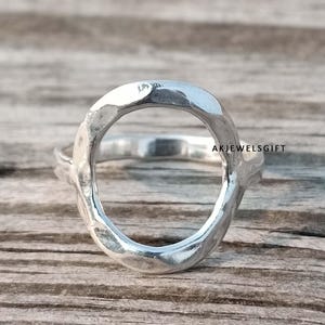 Può includere: Un anello d'argento con un design martellato a forma ovale. L'anello è aperto e ha una finitura liscia e lucida.
